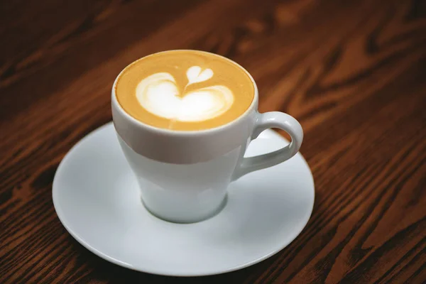 Filiżanka kawy z latte art na drewnianym tle. — Zdjęcie stockowe