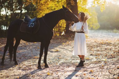 Parkta at ile ayakta kurutulmuş çiçek buketi ile gülümseyen kadın.