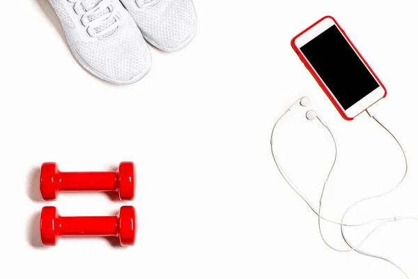 Composition à plat avec baskets, écouteurs, téléphone portable et haltères rouges sur fond blanc . — Photo