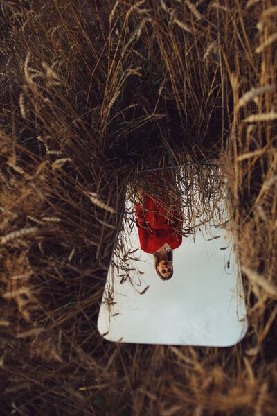 Beautiful woman in red dress in the mirror reflection in the field. — Stock Photo, Image