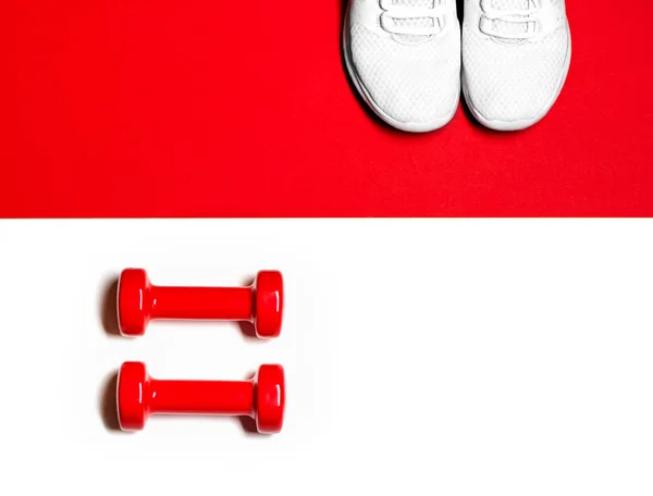 Composition à plat avec haltères rouges et baskets sur fond rouge et blanc . — Photo