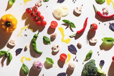 Üst görünüm domates, mürintami, sarı biber, biber, fesleğen, sarımsak ve beyaz arka plan üzerine dökülen zeytinyağı.