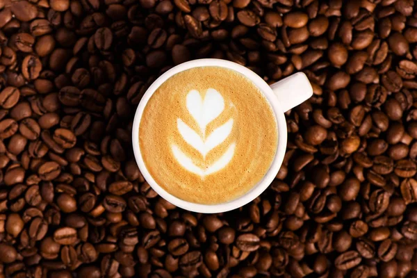 Granos de café tostados fondo con taza de café con arte latte . — Foto de Stock