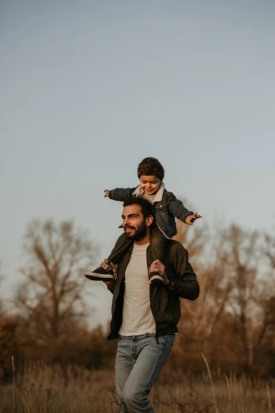 Father giving son ride on his shoulders during countryside walk.
