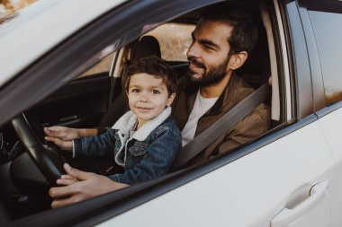 Baba ve küçük oğlu arabada dizlerinin üstünde oturuyorlar..