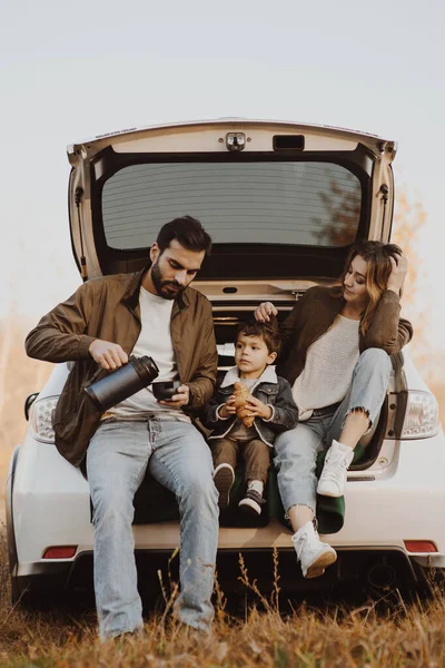 Jeune famille avec mignon fils ayant pique-nique dans le coffre de la voiture . — Photo