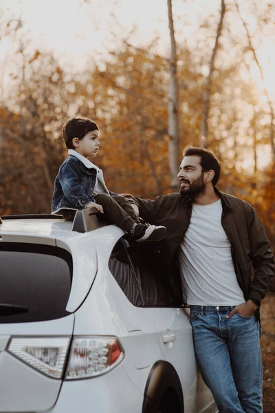 Père heureux debout près de la voiture avec son fils assis sur le toit de la voiture . — Photo