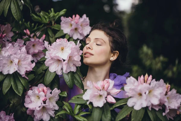 Schöne junge Frau im blühenden Rhododendronbusch. — Stockfoto