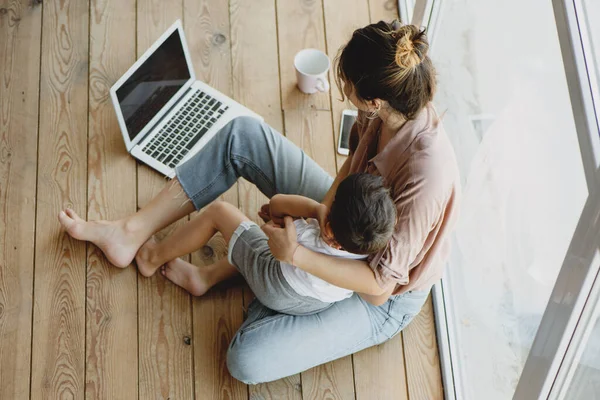 Joven mamá y su hijo sentado en el suelo y mirando a la computadora portátil . — Foto de Stock