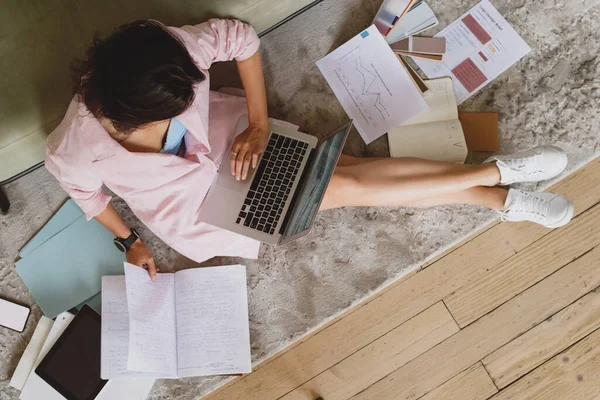 Junge Geschäftsfrau sitzt auf dem Boden und arbeitet mit Dokumenten und tippt auf Laptop. — Stockfoto
