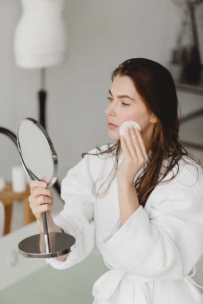 Όμορφη νεαρή γυναίκα χρησιμοποιώντας καλλυντικά σφουγγάρι και κοιτάζοντας τον καθρέφτη. — Φωτογραφία Αρχείου