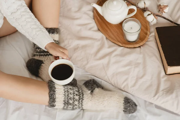 Μερική άποψη της γυναίκας σε πλεκτές κάλτσες στο κρεβάτι με φλιτζάνι καφέ στο χέρι. — Φωτογραφία Αρχείου
