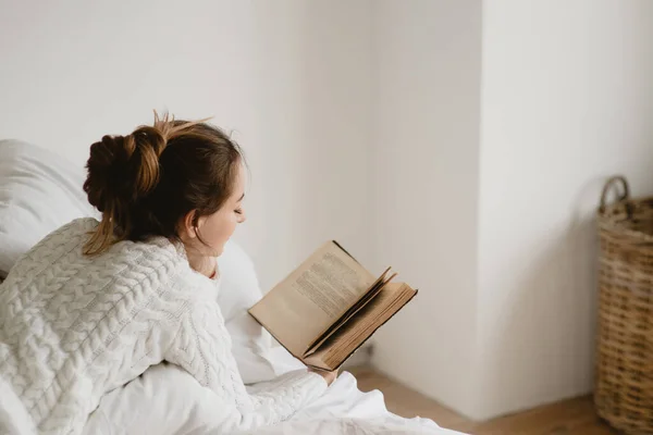 Νεαρή γυναίκα διαβάζει βιβλίο στο κρεβάτι στο σπίτι. — Φωτογραφία Αρχείου