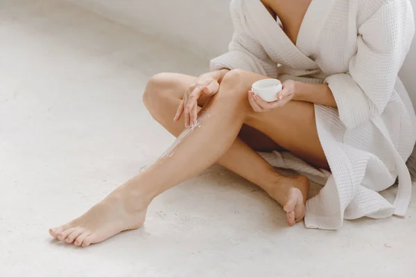 Mujer sentada en la fllor y aplicando crema en las piernas. —  Fotos de Stock
