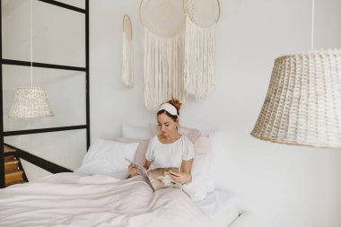 Kadın yatakta uzanıyor ve dergi okuyor..