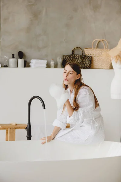 Young woman sitting at bathtub and playing with foam. — Stock Photo, Image