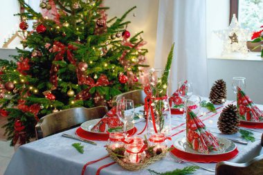 Konforlu ev Noel arifesi, şenlikli masa düzenlemesi ve arka planda Noel ağacı..