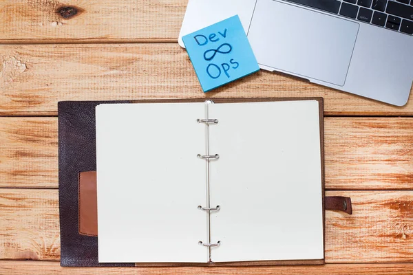 Devops konsepti. Geliştiriciler ve işlemler sözcükler ve semboller, dizüstü bilgisayar, ahşap zemin üzerinde boş sayfalar olan defter. Metnin için boşluk.