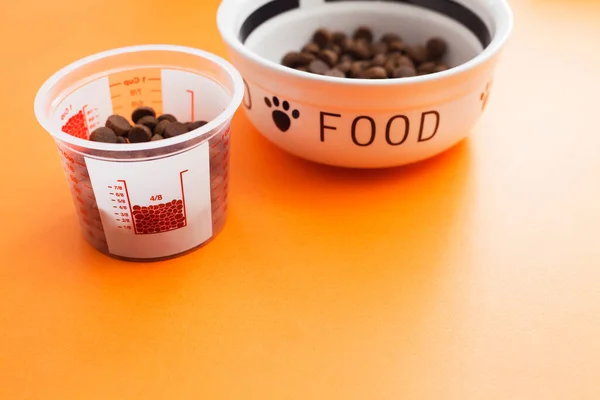 Ölçme kabı, kuru yiyecek kasesi ve turuncu arka planda köpekler için oyuncaklar. Evcil hayvan bakımı, oyun ve antrenman. Üst Manzara. Metin için boşluk.