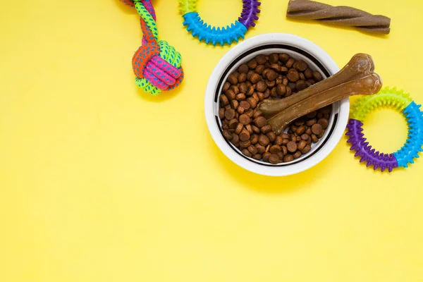 Evcil hayvan bakımı, oyun ve antrenman. Oyuncaklar, aksesuarlar ve kuru yiyecekler sarı arka planda. Üst Manzara. Metin için boşluk.