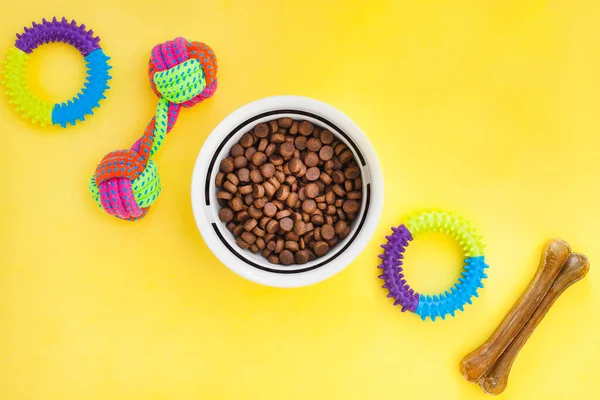 Evcil hayvan bakımı, oyun ve antrenman. Oyuncaklar, aksesuarlar ve kuru yiyecekler sarı arka planda. Üst Manzara. Metin için boşluk.
