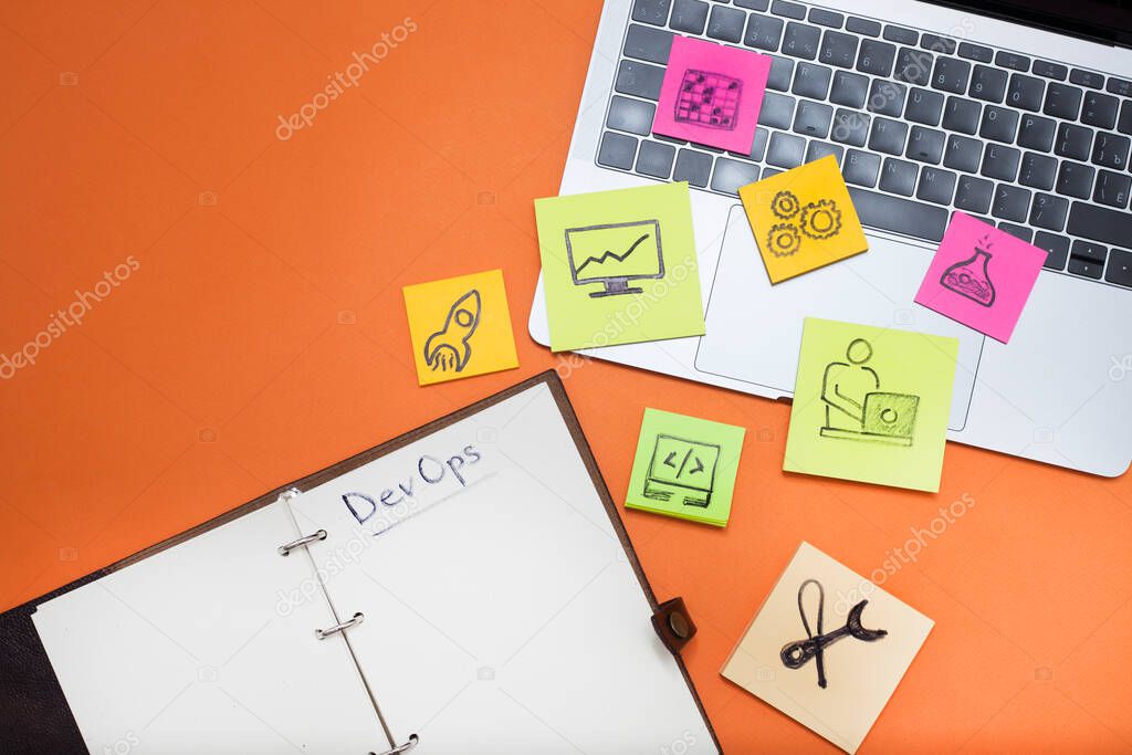 Devops concept. Developers and operations words and symbols, laptop, notebook with blank pages on the orange background. Space for your text.