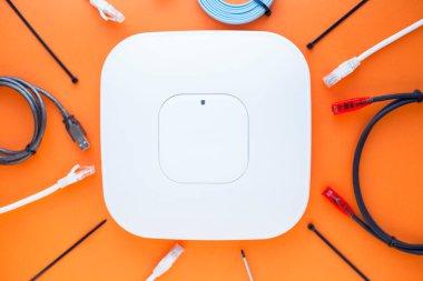 Şirket ağ konsepti. Turuncu arkaplandaki ethernet anahtarları, erişim noktaları, kablolar, bağlayıcılar, dizüstü bilgisayarlar. Üst Manzara. Mesaj atmak için yer var. Kapat..