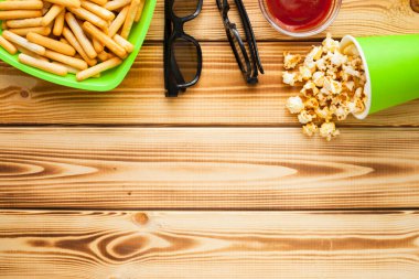 Hafta sonu evde, boş zaman tarzı, TV, fast food konsepti. 3D gözlükler, yeşil kaselerde uzaktan kumanda ve aperatifler: cips, patlamış mısır, ahşap arka planda hamburger. Üst Manzara. Kapat.