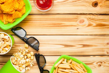 Hafta sonu evde, boş zaman tarzı, TV, fast food konsepti. 3D gözlükler, yeşil kaselerde uzaktan kumanda ve aperatifler: cips, patlamış mısır, ahşap arka planda hamburger. Üst Manzara. Kapat.