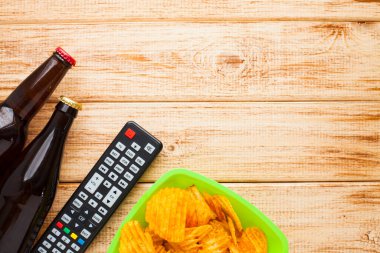 Hafta sonu evde, boş zaman tarzı, TV, fast food konsepti. 3D gözlükler, yeşil kaselerde uzaktan kumanda ve aperatifler: cips, patlamış mısır, ahşap arka planda hamburger. Üst Manzara. Kapat.