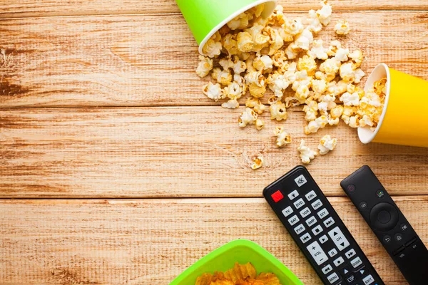 Hafta sonu evde, boş zaman tarzı, TV, fast food konsepti. 3D gözlükler, yeşil kaselerde uzaktan kumanda ve aperatifler: cips, patlamış mısır, ahşap arka planda hamburger. Üst Manzara. Kapat.