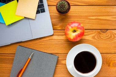 Laptop, beyaz kahve, kaktüs, abur cubur ve parlak ahşap arka planda bir defter. İş, ofis, eğitim, planlama konsepti. Üst Manzara. Kapat..