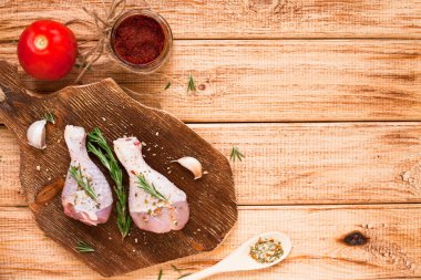 Koyu ahşap kesme tahtasının üzerinde baharatlı, sebzeli ve biberiyeli çiğ tavuk bacağı. Yemek tarifleri, sağlıklı yiyecekler, yaşam tarzı konsepti. Üst Manzara. Kapat..