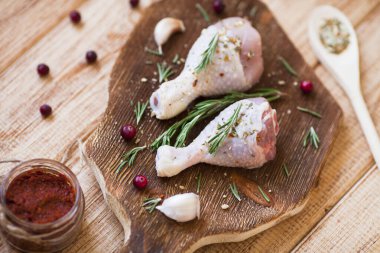 Koyu ahşap kesme tahtasının üzerinde baharatlı, sebzeli ve biberiyeli çiğ tavuk bacağı. Yemek tarifleri, sağlıklı yiyecekler, yaşam tarzı konsepti. Üst Manzara. Kapat..