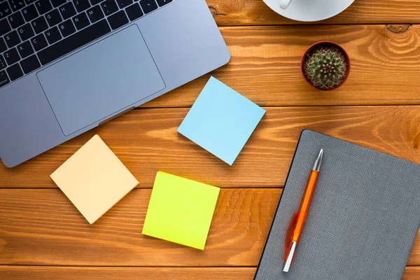 Laptop, beyaz kahve, kaktüs, abur cubur ve parlak ahşap arka planda bir defter. İş, ofis, eğitim, planlama konsepti. Üst Manzara. Kapat..