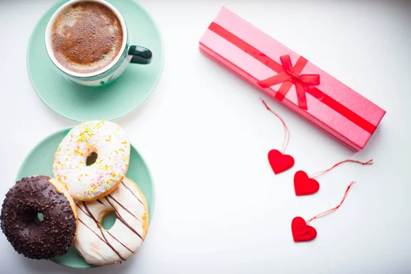 Taze demlenmiş kahve, marşmelov, donut ve tatlı beyaz arka planda. Kurdeleli ve kalpli hediyeler. Üst Manzara. Metnin için boşluk.