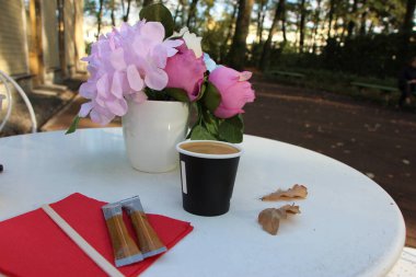 Sonbahar parkındaki terasta yakın plan bir fincan kahve, bir buket çiçek ve iki kahverengi meşe yaprağıyla.