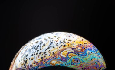 Siyah arka planda izole edilmiş renkli bir sabun köpüğüne yakın, uzaydaki bir gezegene benziyor..