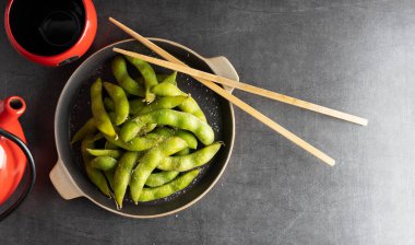 Japon aperatifi Edamame yeşil soya fasulyesi. Tuzlu bir kâse, yanında da çubuklar var..