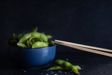 Japon aperatifi Edamame yeşil soya fasulyesi. Tuzlu bir kâse, yanında da çubuklar var..