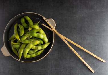 Japon aperatifi Edamame yeşil soya fasulyesi. Tuzlu bir kâse, yanında da çubuklar var..