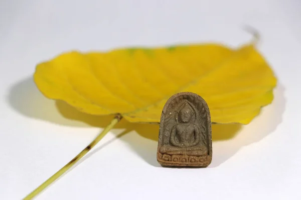 白い床に黄色い神聖なイチジクや菩提樹の葉を持つ小さな仏像のお守り 心臓へのアンカーの使用 — ストック写真