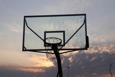Şeffaf duvar silueti monte edilmiş ve güneş doğarken gökyüzü arka planında ağ olan basketbol potası..