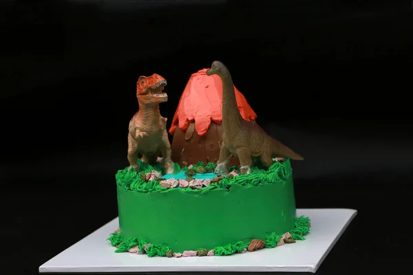 两个恐龙娃娃装饰在一个火山蛋糕上 一个绿色森林的地方装饰在一个黑色背景的白色正方形盘子上 — 图库照片