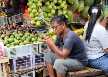 Jakarta, Endonezya 2 Mayıs 2019: Endonezyalı adam Cakarta 'daki yeni marketin önünde oturuyor ve cep telefonu kullanıyor.