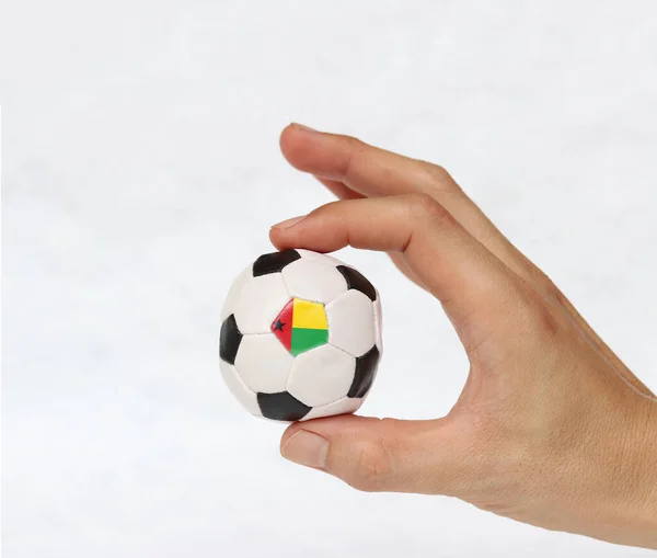 手拿着小球和一个黑点的足球是几内亚比索旗 用两根手指在白色背景上握住它 体育运动的概念或操纵性或次要事物中的游戏 — 图库照片
