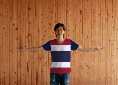 Tayland bayraklı gömlek giyen ve kolları açık duran adam ahşap duvar zemininde, yatay beyaz, kırmızı ve mavi renkli..