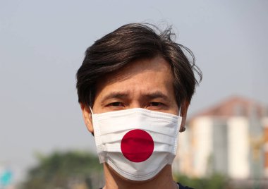Japon bayrağı hijyen maskesinde. Maskeli Asyalı adam mikropları engeller. Tiny Partikül koruması veya virüs koronası kavramı.
