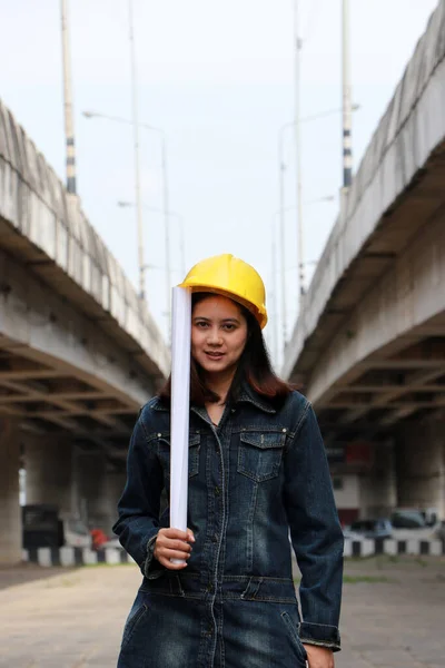 具有黄色头盔的女土木工程师或建筑师 在平行高速公路背景下手握项目草案站立 — 图库照片
