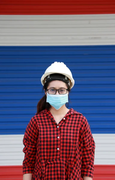 Female civil engineer or architect with white helmet and masked prevent germs, wear red plaid dress on the color of Thailand flag door background. Tiny Particle or virus corona or Covid 19 protection.